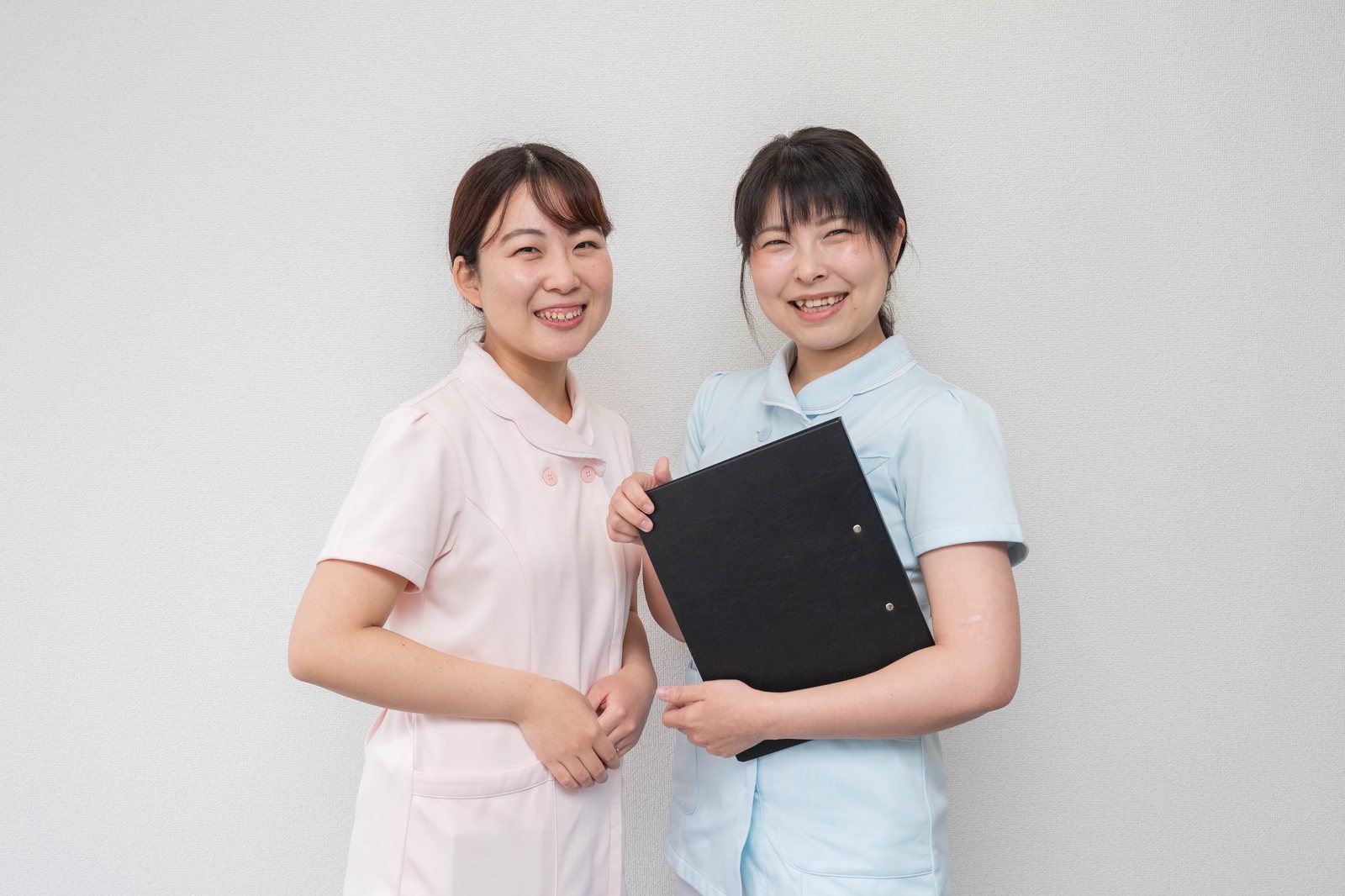 クリップボードを手に笑顔で並ぶ歯科助手のスタッフ